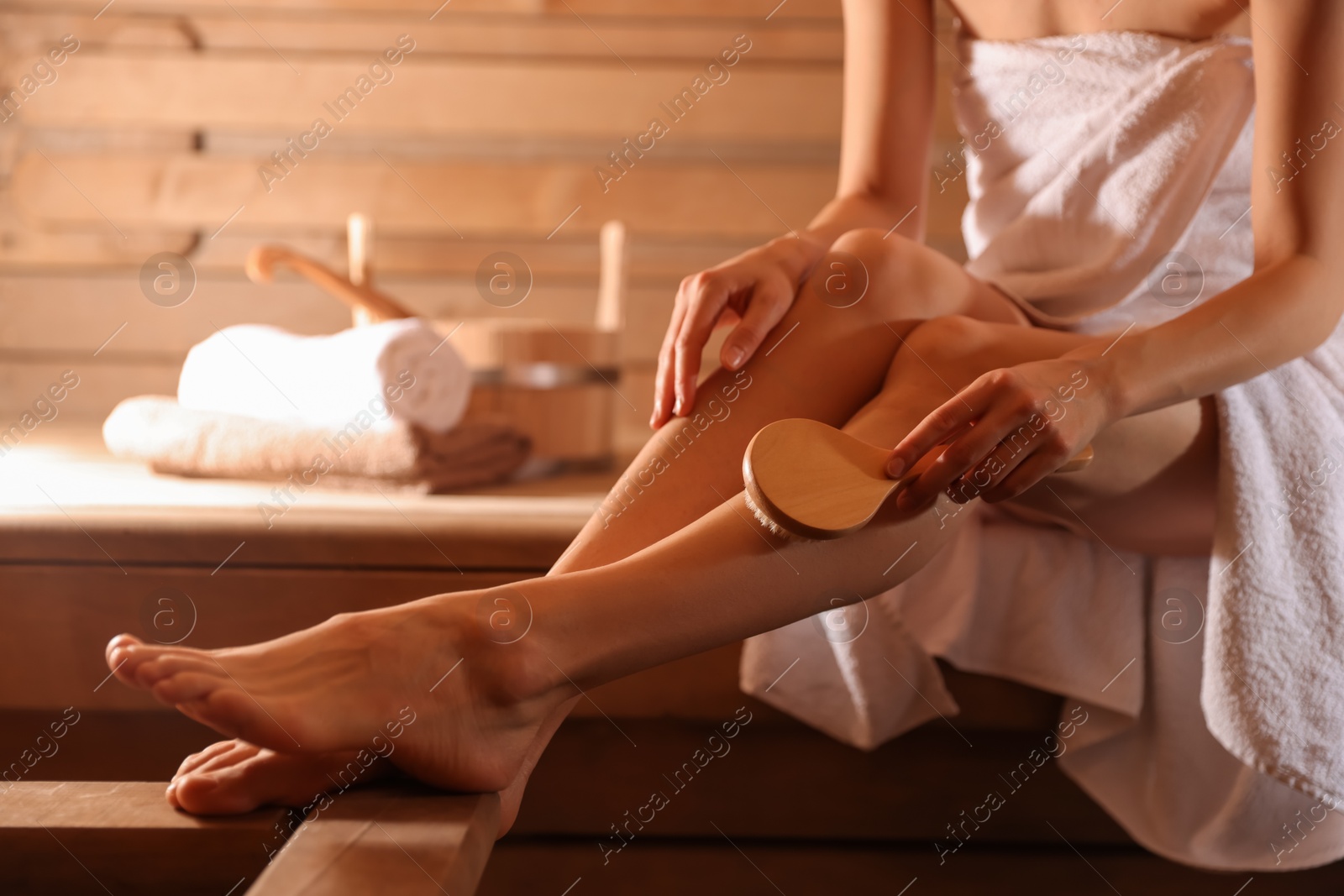 Photo of Woman massaging her leg with brush at sauna, closeup