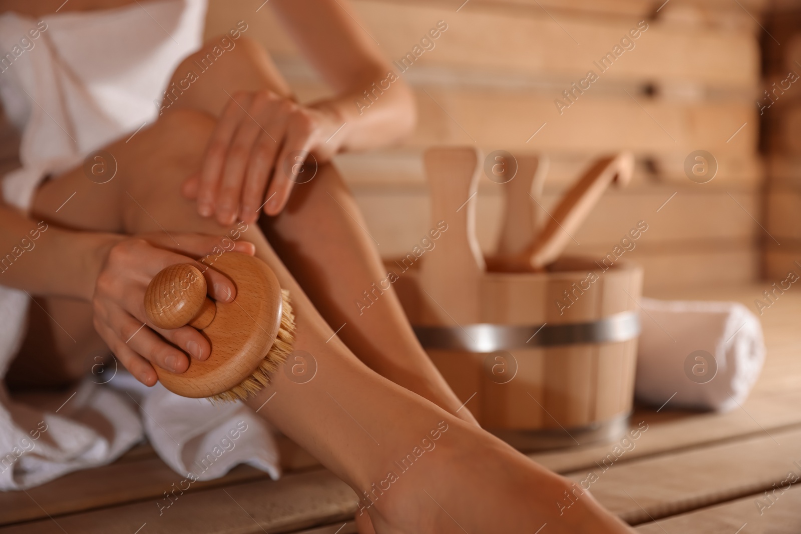 Photo of Woman massaging her leg with brush and bath supplies at sauna, closeup