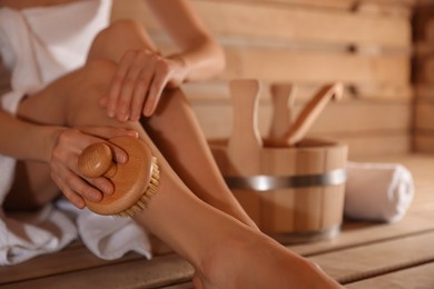 Photo of Woman massaging her leg with brush and bath supplies at sauna, closeup