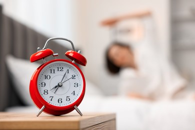 Photo of Young woman exercising on bed at home, focus on alarm clock. Morning routine