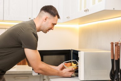 Photo of Man putting container with lunch into microwave in kitchen