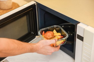 Photo of Man putting container with lunch into microwave in kitchen, closeup