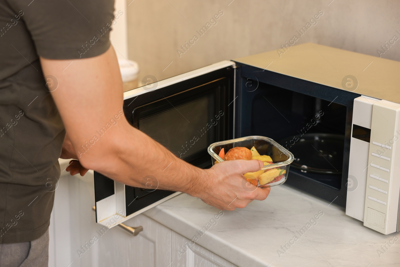 Photo of Man putting container with lunch into microwave in kitchen, closeup