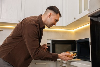 Photo of Man putting container with lunch into microwave in kitchen