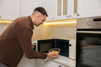 Photo of Man putting container with lunch into microwave in kitchen