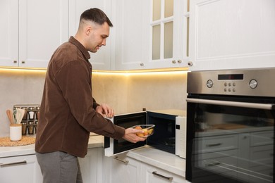 Photo of Man putting container with lunch into microwave in kitchen