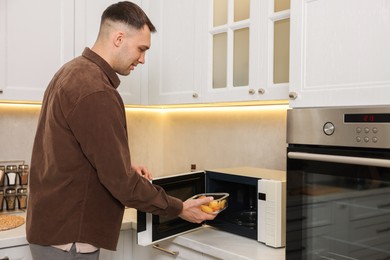 Photo of Man putting container with lunch into microwave in kitchen