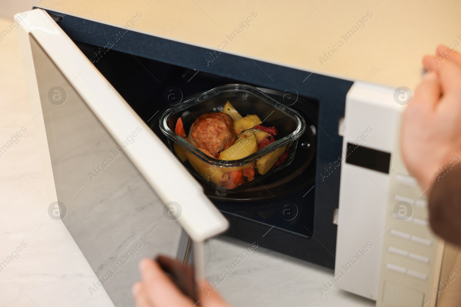 Photo of Man putting container with lunch into microwave in kitchen, closeup