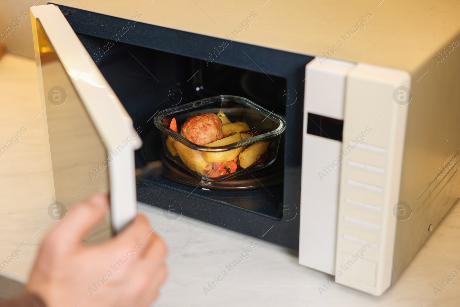 Photo of Man putting container with lunch into microwave in kitchen, closeup