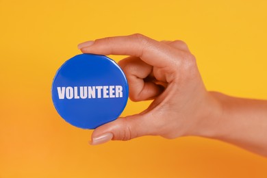 Woman showing blue button badge with word Volunteer on orange background, closeup