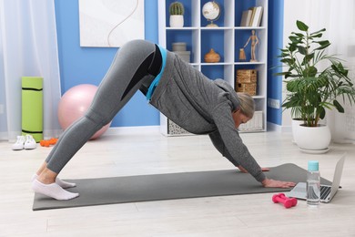 Elderly woman exercising near laptop at home