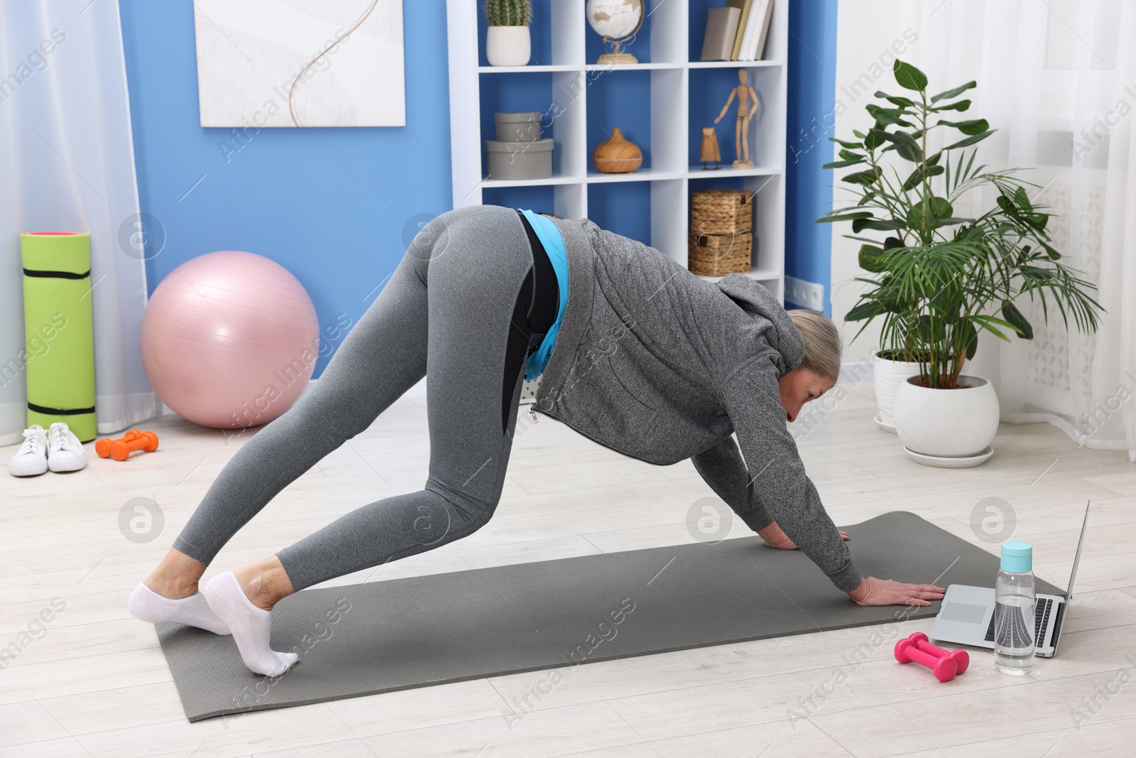 Photo of Elderly woman exercising near laptop at home