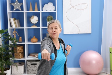 Photo of Elderly woman exercising with dumbbells at home