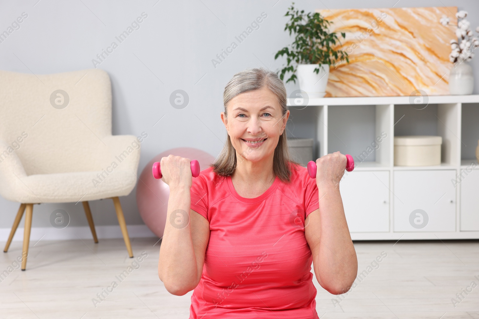 Photo of Smiling elderly woman exercising with dumbbells at home