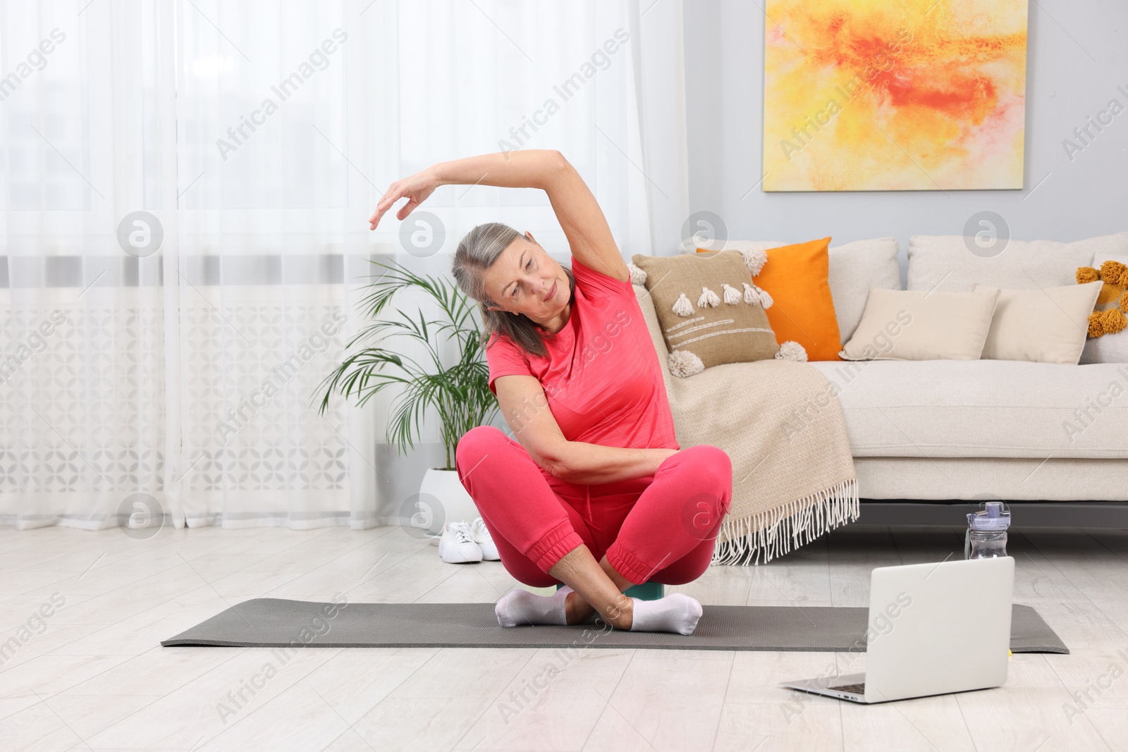 Photo of Elderly woman exercising near laptop at home