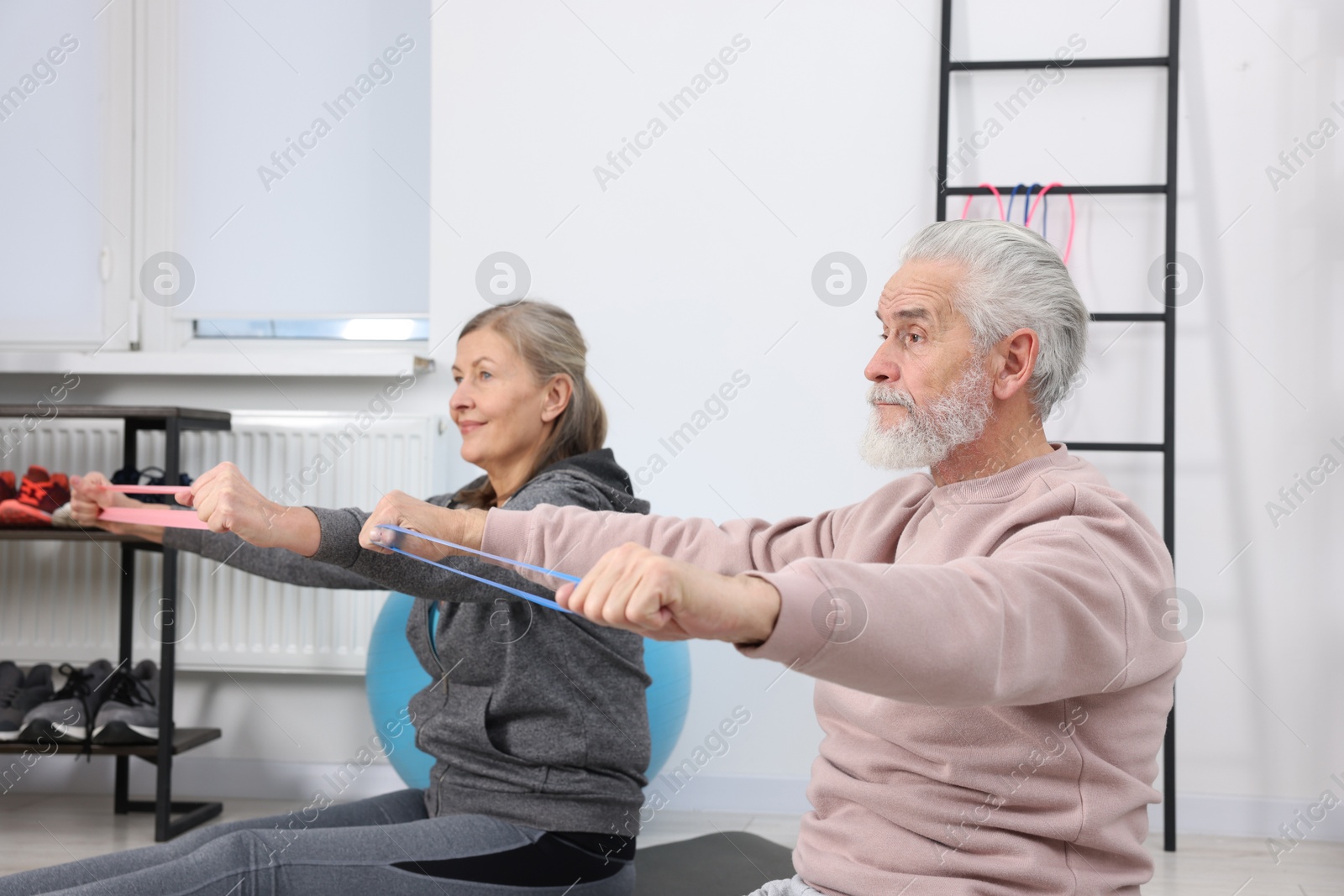 Photo of Elderly couple exercising with fitness elastic bands at home