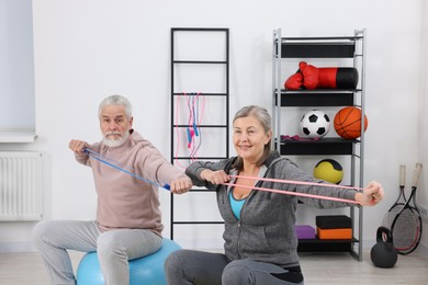 Elderly couple exercising with elastic bands and fitness balls at home