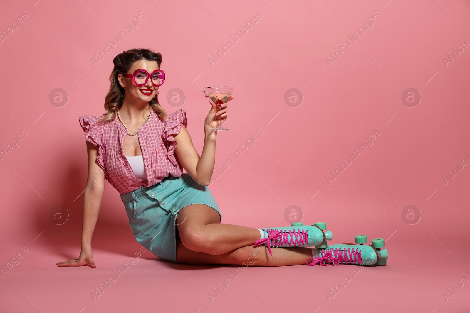 Photo of Happy pin-up woman wearing roller skates with cocktail on pink background, space for text