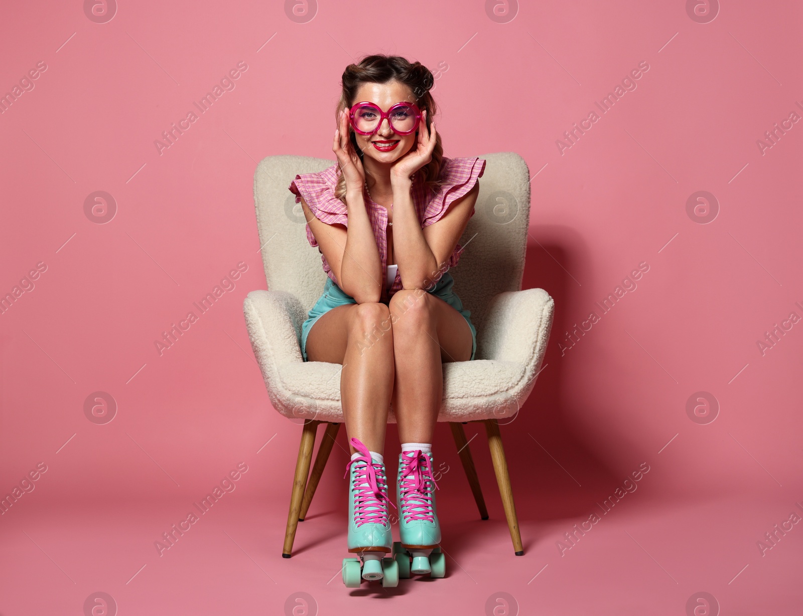 Photo of Happy pin-up woman in roller skates sitting on armchair against pink background