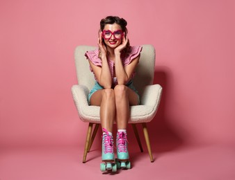 Happy pin-up woman in roller skates sitting on armchair against pink background