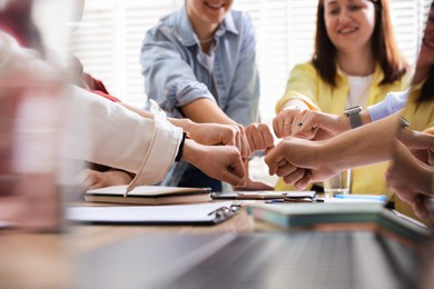 Photo of Unity concept. People holding fists together at table indoors, closeup