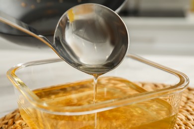 Photo of Pouring used cooking oil into glass container at white table, closeup