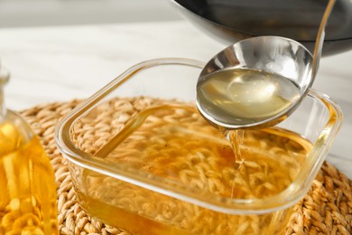 Photo of Pouring used cooking oil into glass container at white table, closeup