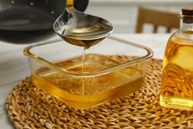 Photo of Pouring used cooking oil into glass container at white table, closeup