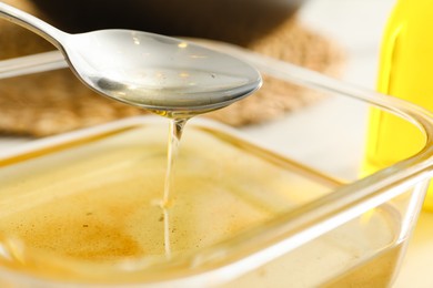 Photo of Pouring used cooking oil into glass container at white table, closeup