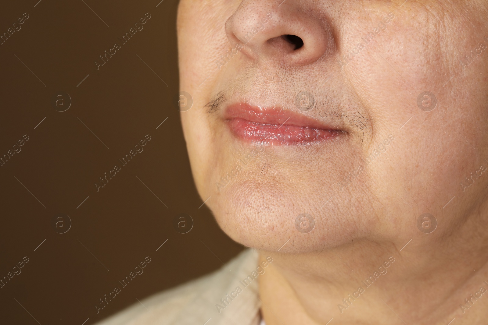 Photo of Senior woman with mustache on brown background, closeup. Space for text