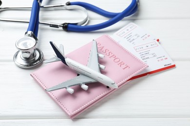 Photo of Medical tourism. Stethoscope, plane model, passport and flight tickets on white wooden table, closeup