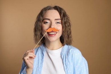 Happy woman with fake paper mustache on beige background