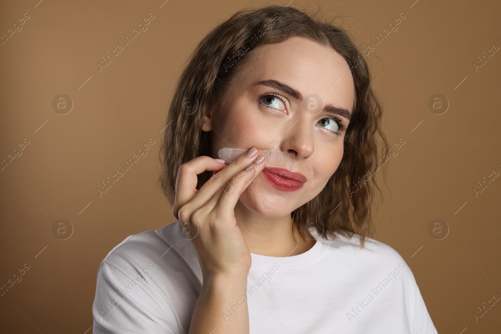 Photo of Beautiful woman removing her mustache with wax strip on beige background