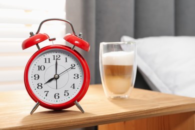 Photo of Alarm clock and coffee on nightstand near bed