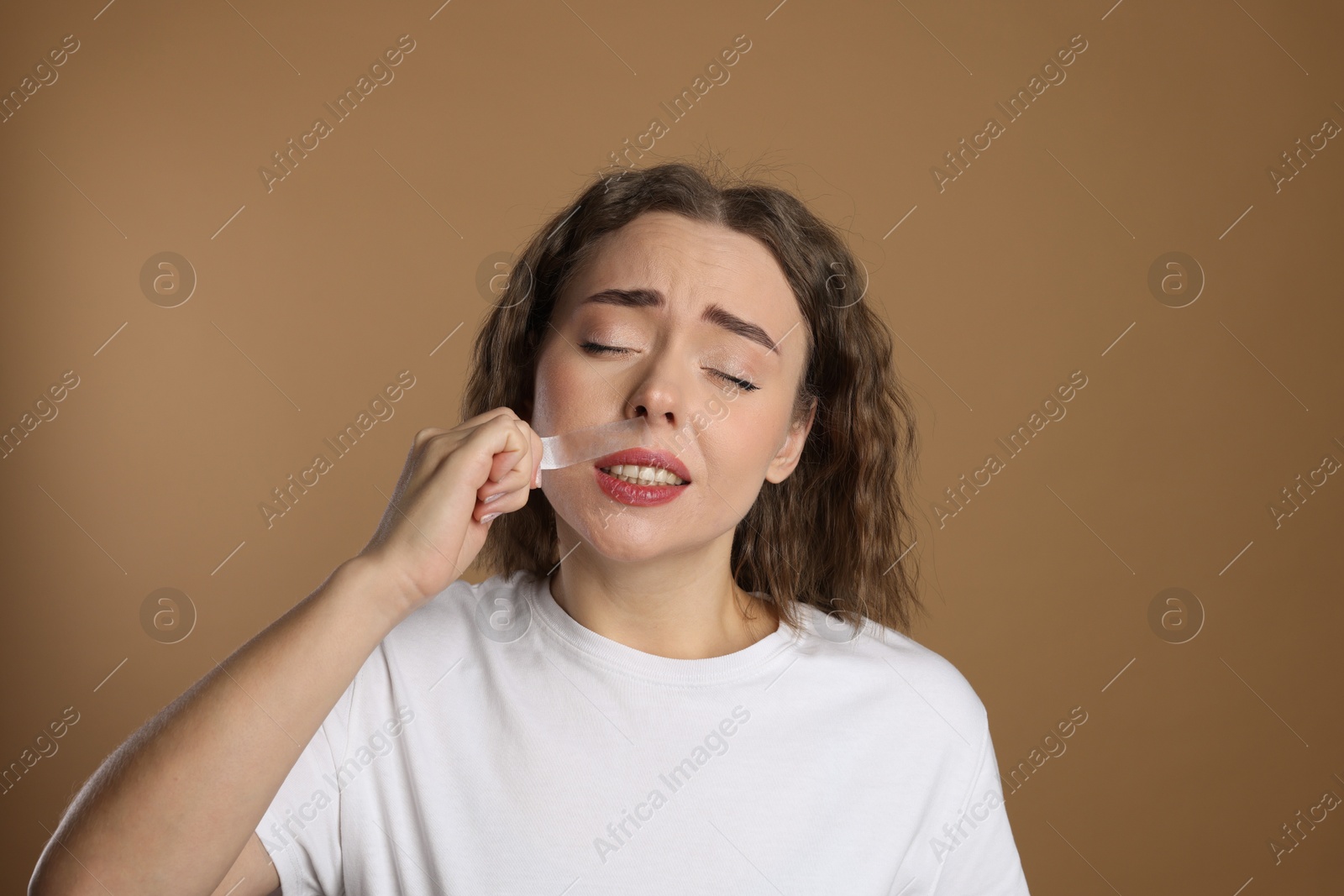 Photo of Emotional woman removing her mustache with wax strip on beige background