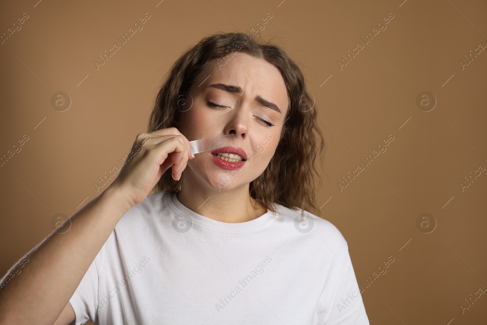 Photo of Emotional woman removing her mustache with wax strip on beige background