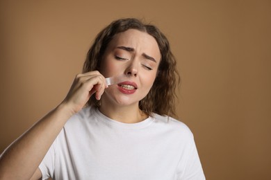 Photo of Emotional woman removing her mustache with wax strip on beige background