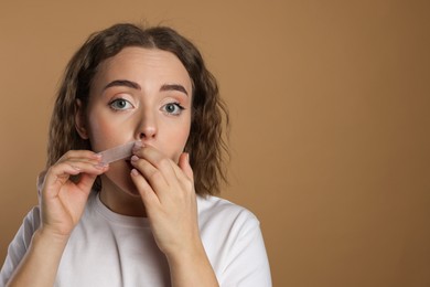 Photo of Emotional woman removing her mustache with wax strip on beige background. Space for text