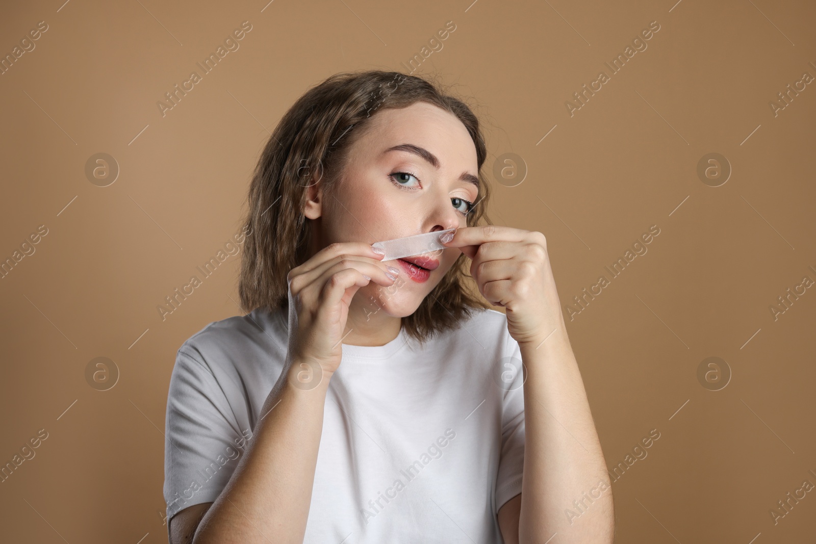 Photo of Emotional woman removing her mustache with wax strip on beige background