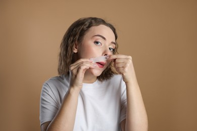 Emotional woman removing her mustache with wax strip on beige background