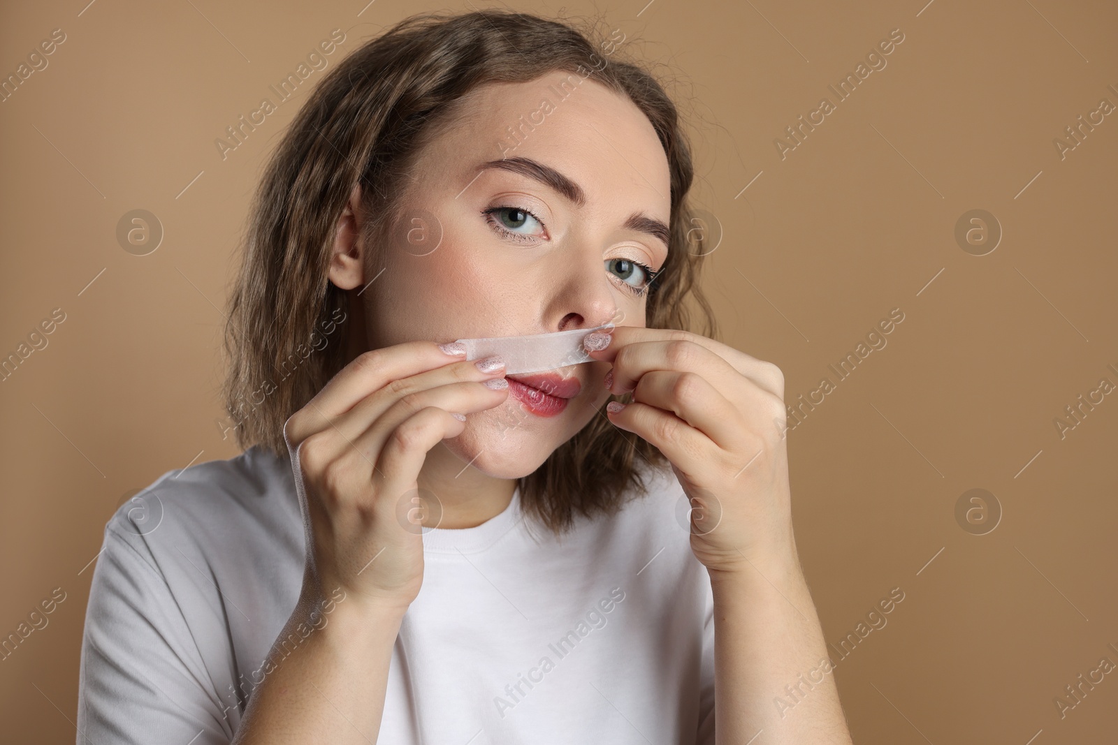 Photo of Emotional woman removing her mustache with wax strip on beige background