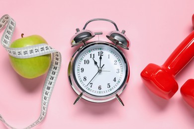 Photo of Alarm clock, dumbbells, apple and measuring tape on pink background, flat lay