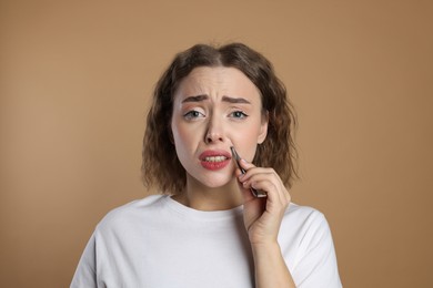 Disappointed woman plucking her mustache with tweezers on beige background