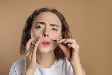 Beautiful woman plucking her mustache with tweezers on beige background