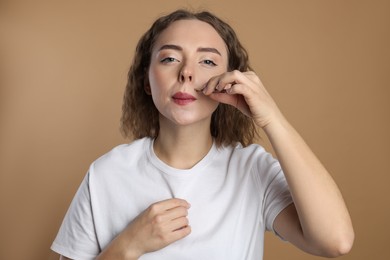 Photo of Beautiful woman plucking her mustache with tweezers on beige background