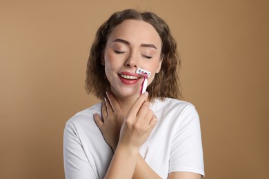 Smiling woman shaving her mustache with razor on beige background