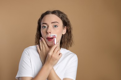 Photo of Beautiful woman shaving her mustache with razor on beige background. Space for text