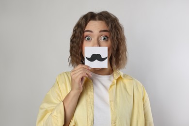 Woman holding paper with drawn mustache on grey background