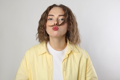 Funny woman making mustache from her hair on grey background