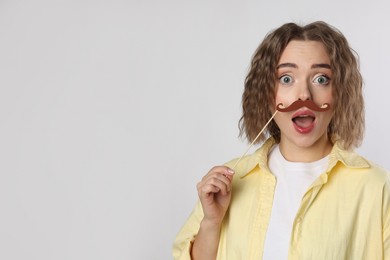 Emotional woman with fake paper mustache on grey background. Space for text